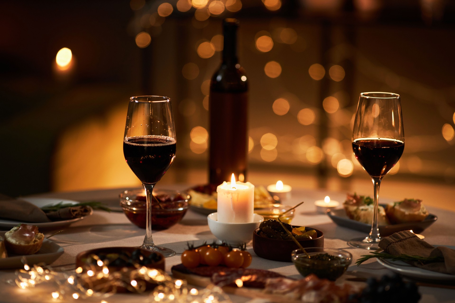 Two wine glasses on dinner table with Christmas lights and candles